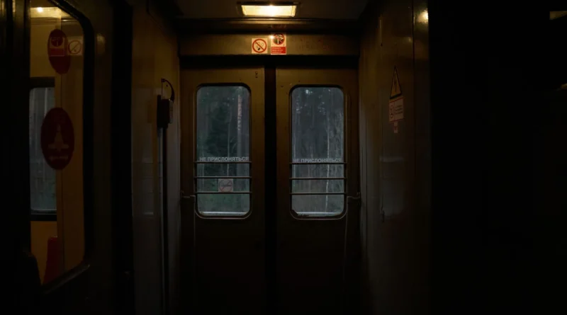 Interior de um trem noturno com bancos azuis vazios e luz amarelada entrando pela janela