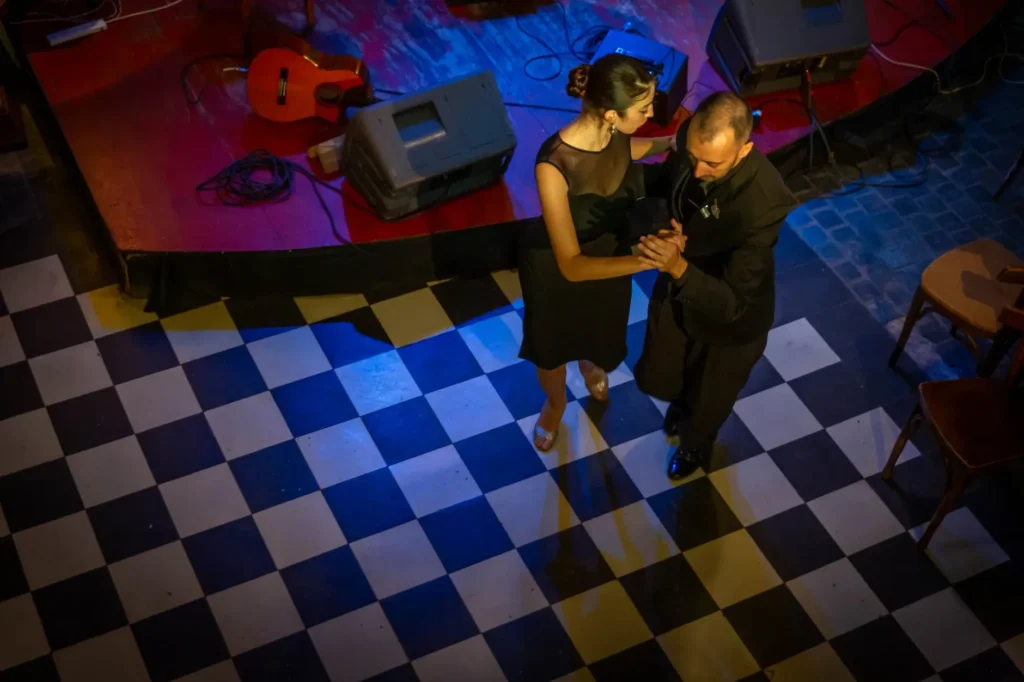 Casal de adultos abraçado numa milonga de tango sob luz âmbar