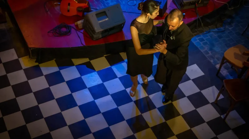 Casal de adultos abraçado numa milonga de tango sob luz âmbar