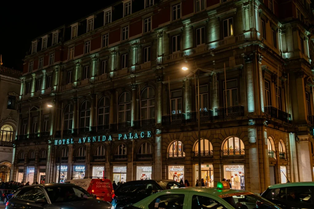 Varanda de hotel à noite com luzes da cidade ao fundo, duas taças sobre a mesa, ambiente elegante e reservado.