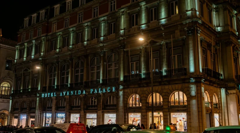 Varanda de hotel à noite com luzes da cidade ao fundo, duas taças sobre a mesa, ambiente elegante e reservado.