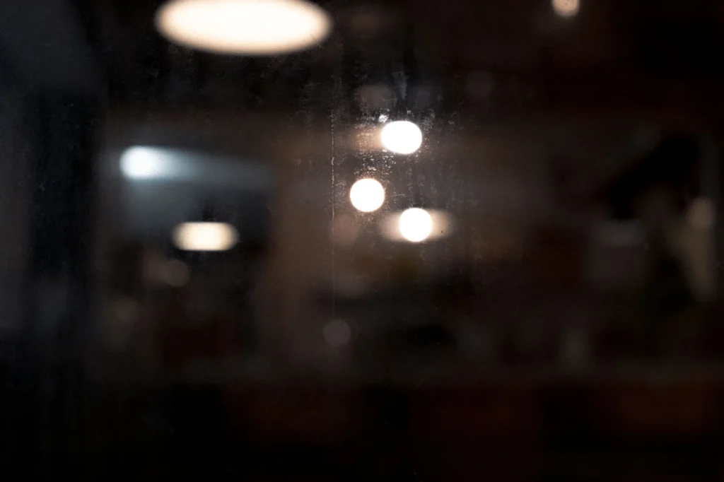 Recepção de academia vazia à noite, com luz amarelada baixa, balcão de madeira e chuva escorrendo na janela, ambiente silencioso frequentado apenas por adultos
