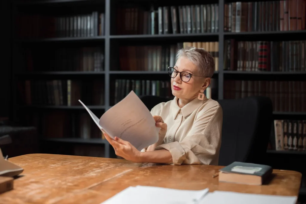 Duas pessoas adultas leem um manuscrito à luz quente de uma biblioteca à noite