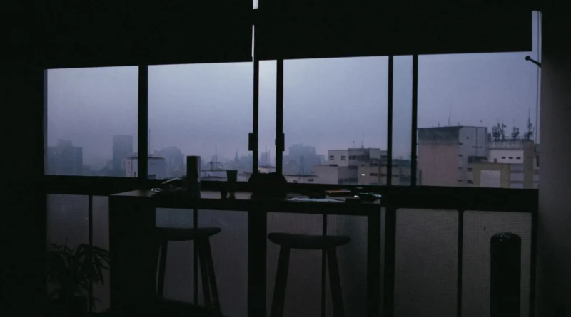 Duas chávenas de café sobre uma mesa de madeira numa varanda de prédio ao anoitecer, ambiente calmo e reservado sem pessoas