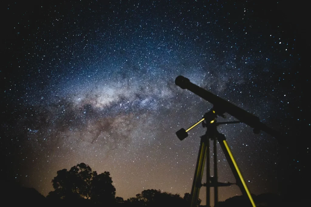 Telescópio debruçado sobre um céu estrelado de outono na serra, com duas mantas vazias no gramado ao lado