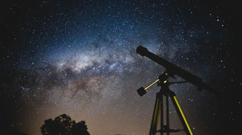 Telescópio debruçado sobre um céu estrelado de outono na serra, com duas mantas vazias no gramado ao lado