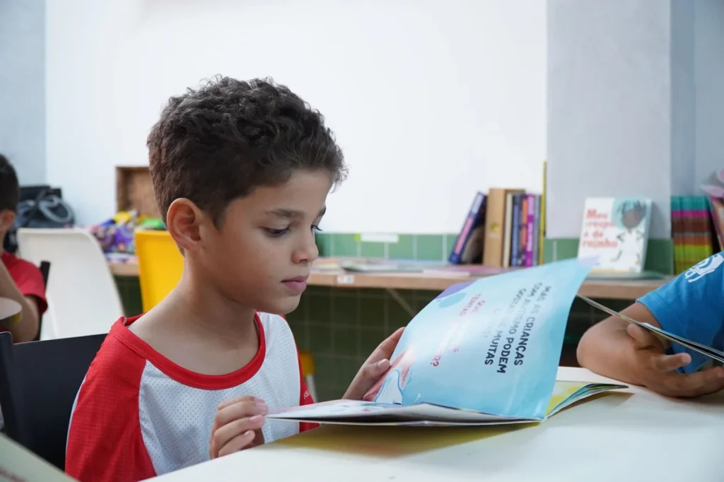 Dois adultos leem livros juntos à mesa sob a luz quente de um abajur