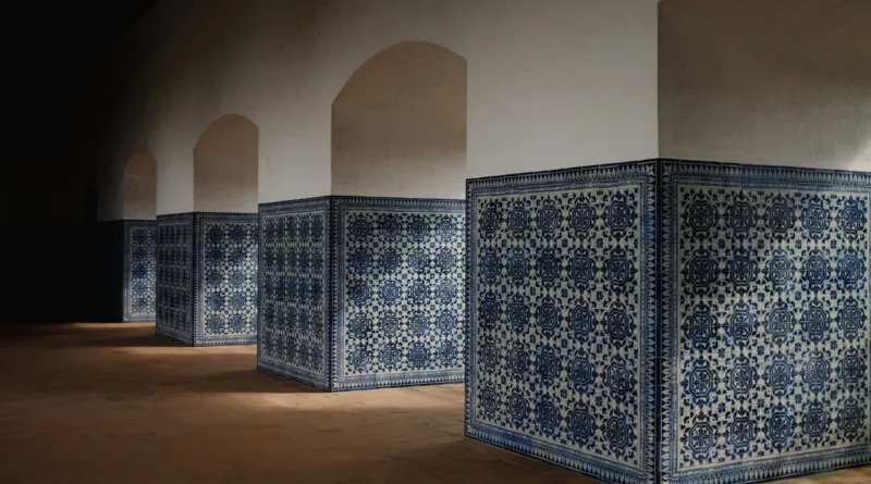 Duas pessoas adultas observam juntas um painel de azulejos restaurado numa oficina iluminada em Lisboa